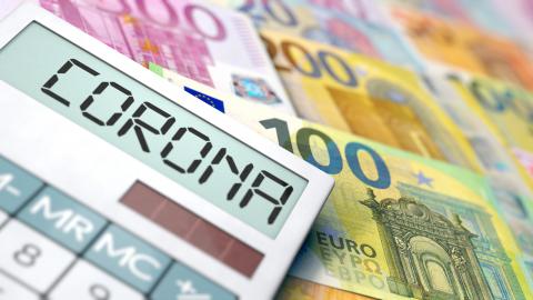 Finanzielle Unterstützung in Zeiten der Corona-Krise. Ein Taschenrechner mit dem Wort Corona im Display und unter ihm liegen Geldscheine.