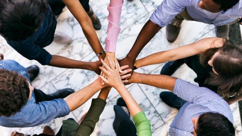 Gemeinsam ist man stärker. Mehrere Menschen stehen im Kreis und legen ihre Hände aufeinander.