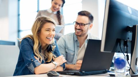 Zwei Mitarbeiterinnen und ein Mitarbeiter gut gelaunt am Schreibtisch.