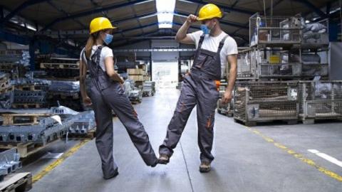 Zwei Fabrikarbeiter, die sich mit den Füßen begrüßen.