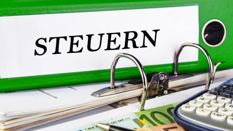 Ein Aktenordner mit der Aufschrift "Steuern" sowie ein Taschenrechner und Geldscheine. Ein Aktenordner mit der Aufschrift "Steuern" sowie ein Taschenrechner und Geldscheine.