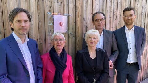 Plakette zur Auszeichnung Vorbildliche Bauten in Hessen 2023 Finanzminister Boddenberg (4. vl.l) steht gemeinsam mit Marcus Gwechenberger ( links im Bild), Brigitte Holz (2. v.l.), Christine Heinrichs (3. v.l.) und Architekt Marco Schlothauer (rechts im Bild) vor einer Wand, auf der die Plakette zur Auszeichnung Vorbildliche Bauten in Hessen 2023 angebracht ist.