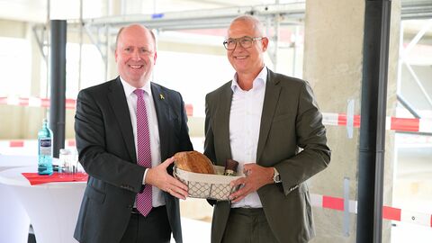 Hessens Finanzstaatssekretär Uwe Becker (links im Bild) freut sich beim Richtfest gemeinsam mit dem Leiter des Finanzamts Limburg-Weilburg, Andreas Wendland, über die Baufortschritte beim zukünftigen Dienstgebäude und überreicht ihm Brot und Salz. 