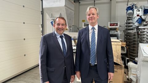 FInanzminister Lorz steht neben Manfred Schultheis in einer Produktionshalle, beide lächeln. Im Hintergrund sind Maschinen zu sehen.