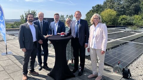 Finanzminister Lorz steht mit weiteren Personen um einen Stehtisch auf einer Dachterrasse. Im Hintergrund ist eine Photovoltaikanlage zu sehen.