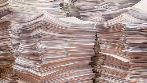 Ein hoher bürokratischer Aufwand sollte vermieden werden. Zu sehen sind mehrere hohe Papierstapel.