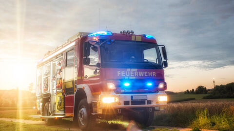 Sie helfen, wenn es brennt: Die Freiwilligen Feierwehren leisten unverzichtbare Arbeit zum Schutz der Bürgerinnen und Bürger. Ein Feuerwehrauto fährt in der Dämmerung auf einem Feldweg.