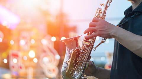 Zu sehen ist im Bildvordergrund ein Jazzmusiker mit Saxophon, im Bildhintergrund eine Bühne.
