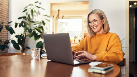 Der Chatbot auf finanzamt.hessen.de hilft Bürgerinnen und Bürgern bei allgemeinen Steuerfragen weiter. Eine Frau sitzt an einem Tisch und arbeitet an einem Laptop.