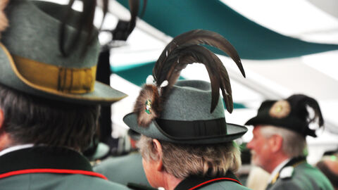 Zu sehen sind die Rückansichten von drei Schützen in Uniform bei einer Feierlichkeit.