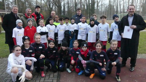 Hessens Finanzminister Professor Dr. R. Alexander Lorz überreicht den Förderbescheid an den Fußballverein Delkenheim. Mit ihm freuen sich der Erste Vorsitzende des Vereins, Ömür Yalciner, Jugendleiter Markus Christ und weitere Mitglieder des Vereinsvorstandes sowie die E1-Jugend des FV Delkenheim, die gegen die U11-Juniorinnen-Mannschaft von Mainz 05 antrat.
