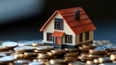 Grundsteuer Zu sehen ist das Modell eines Hauses im Bildhintergrund. Im Bildvordergrund liegen Münzen.