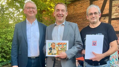 Finanzminister Lorz (mitte) überreicht den Lottobescheid über 1165 Euro an die Interessensgemeinschaft Weinstand Igstadt. 