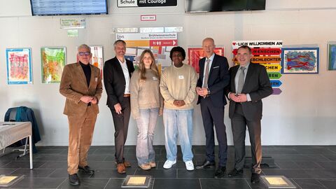 Von links nach rechts zu sehen sind der Vorstand der Verbraucherzentrale Hessen, Philipp Wendt, der Schulleiter der Brühlwiesenschule, Christoph Berg, eine Schülerin und ein Schüler der Brühlwiesenschule, Hessens Kultusminister Armin Schwarz und Finanzminister Professor Dr. R. Alexander Lorz. Sechs Personen, darunter auch zwei Schüler, stehen nebeneinander in einem Klassenraum.