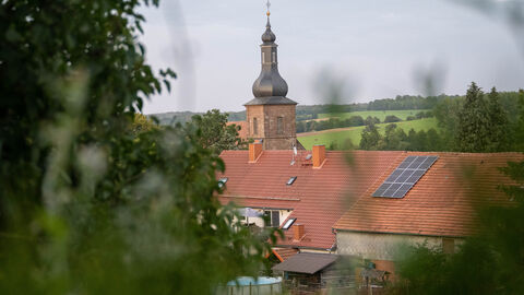 Blick auf Häuserdächer und einen Kirchturm in grüner Landschaft.